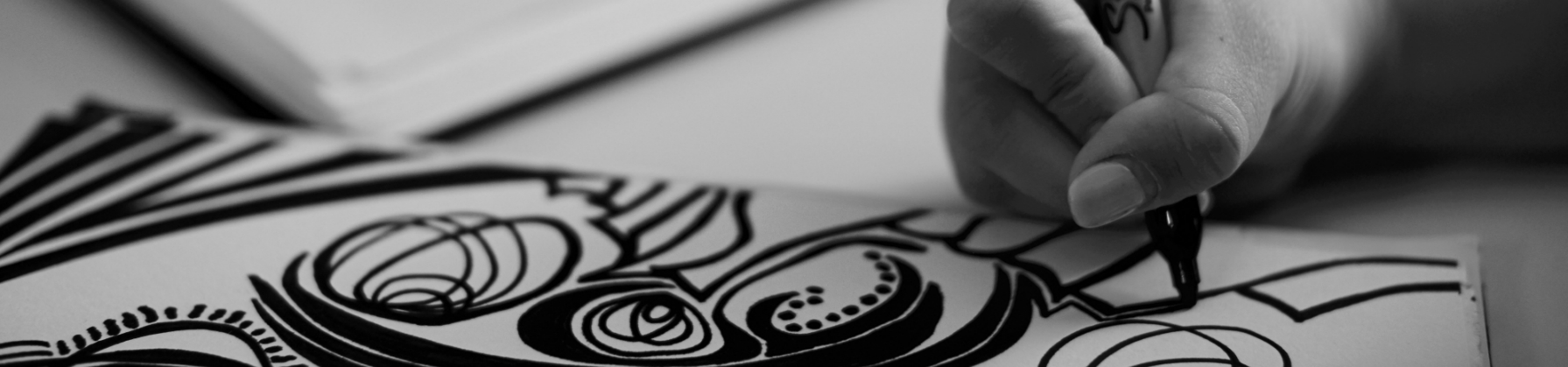 A hand is drawing a design on paper with a black sharpie marker.