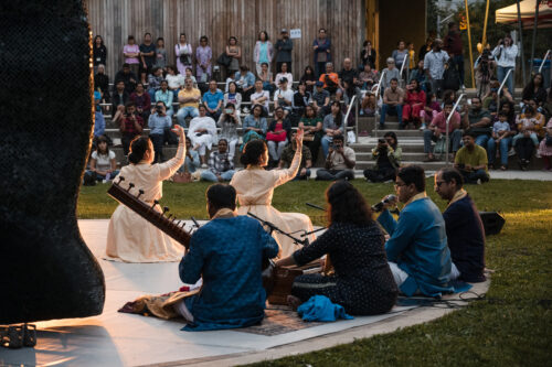 Artists perform on an outdoor stage to a group of captivated audience members