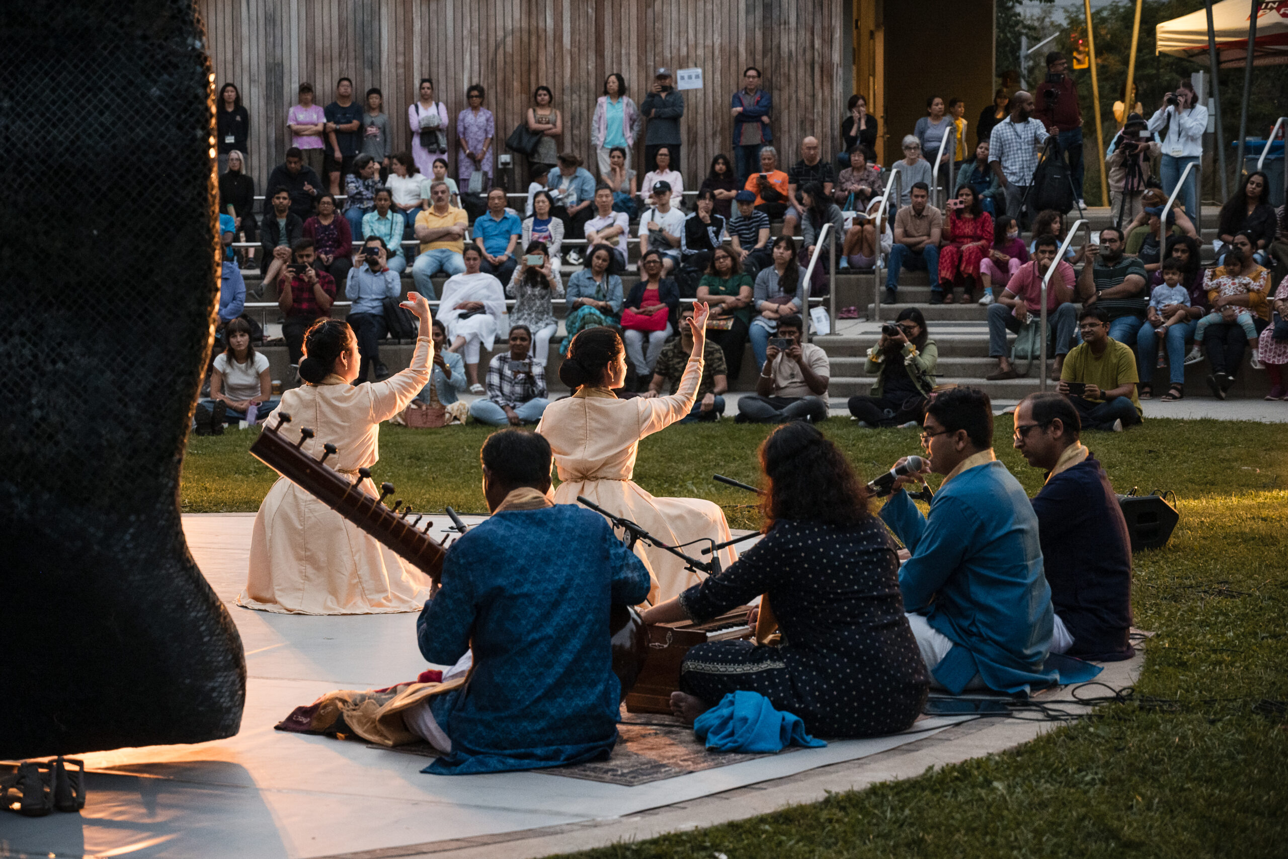 Artists perform on an outdoor stage to a group of captivated audience members