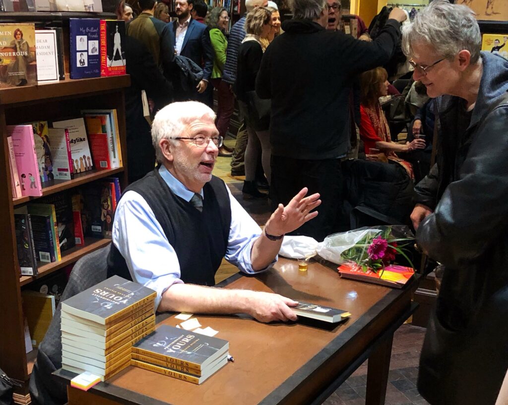 Antanas Sileika sits at a table speaking to a fan at a book launch