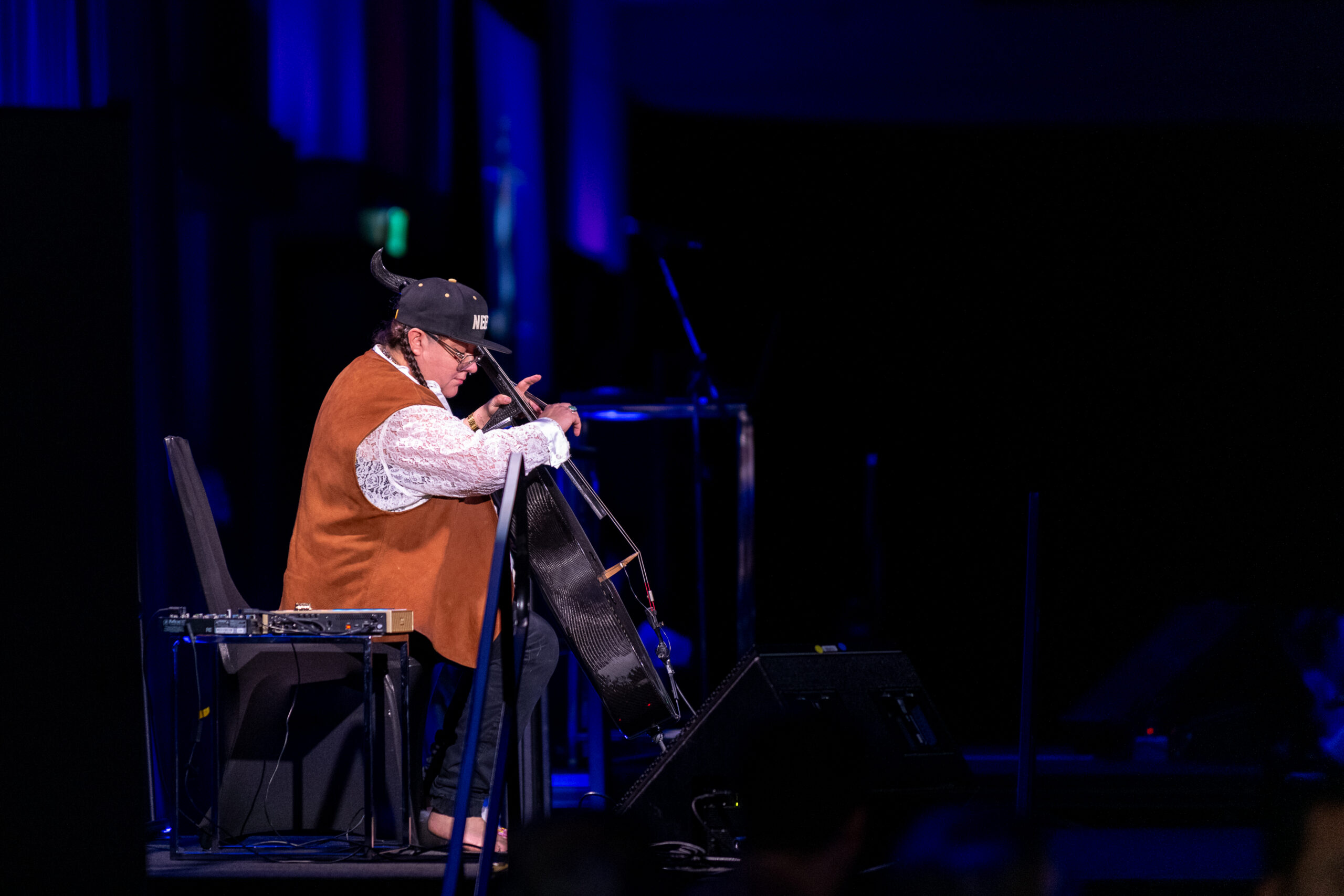 A photo of Cris Derksen playing cello on a dark stage