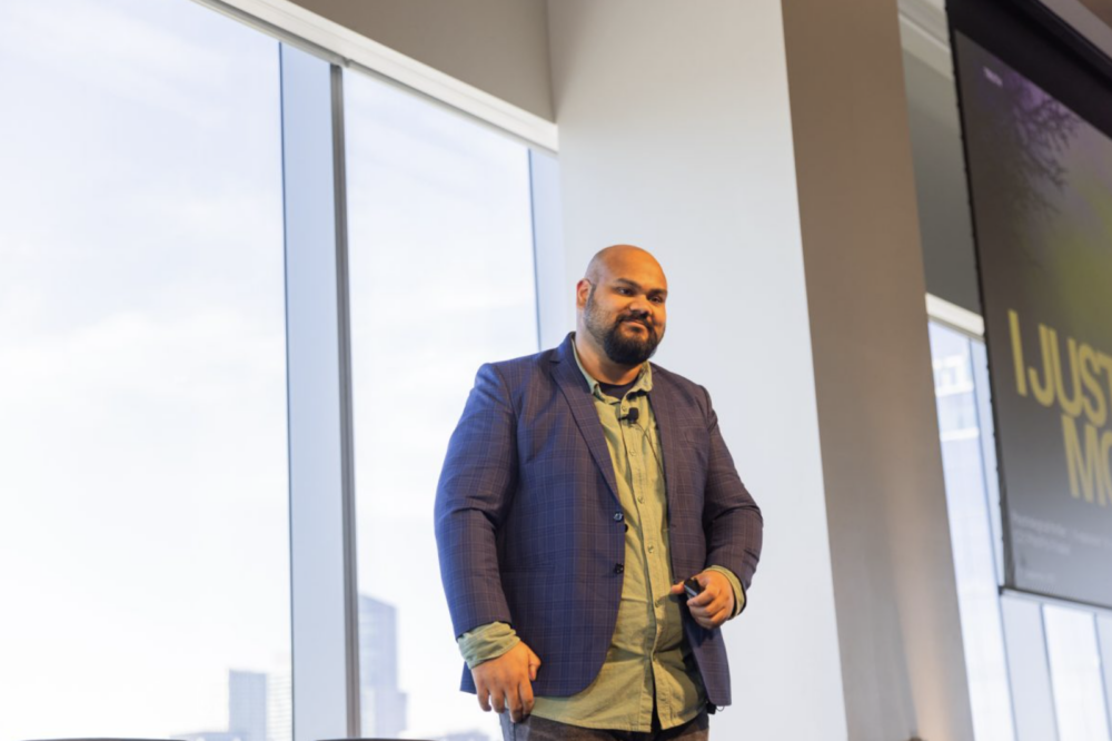 Gursimran Datla stands on stage in a suit.