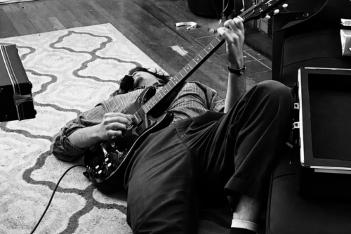 A person lies on a rug playing guitar.